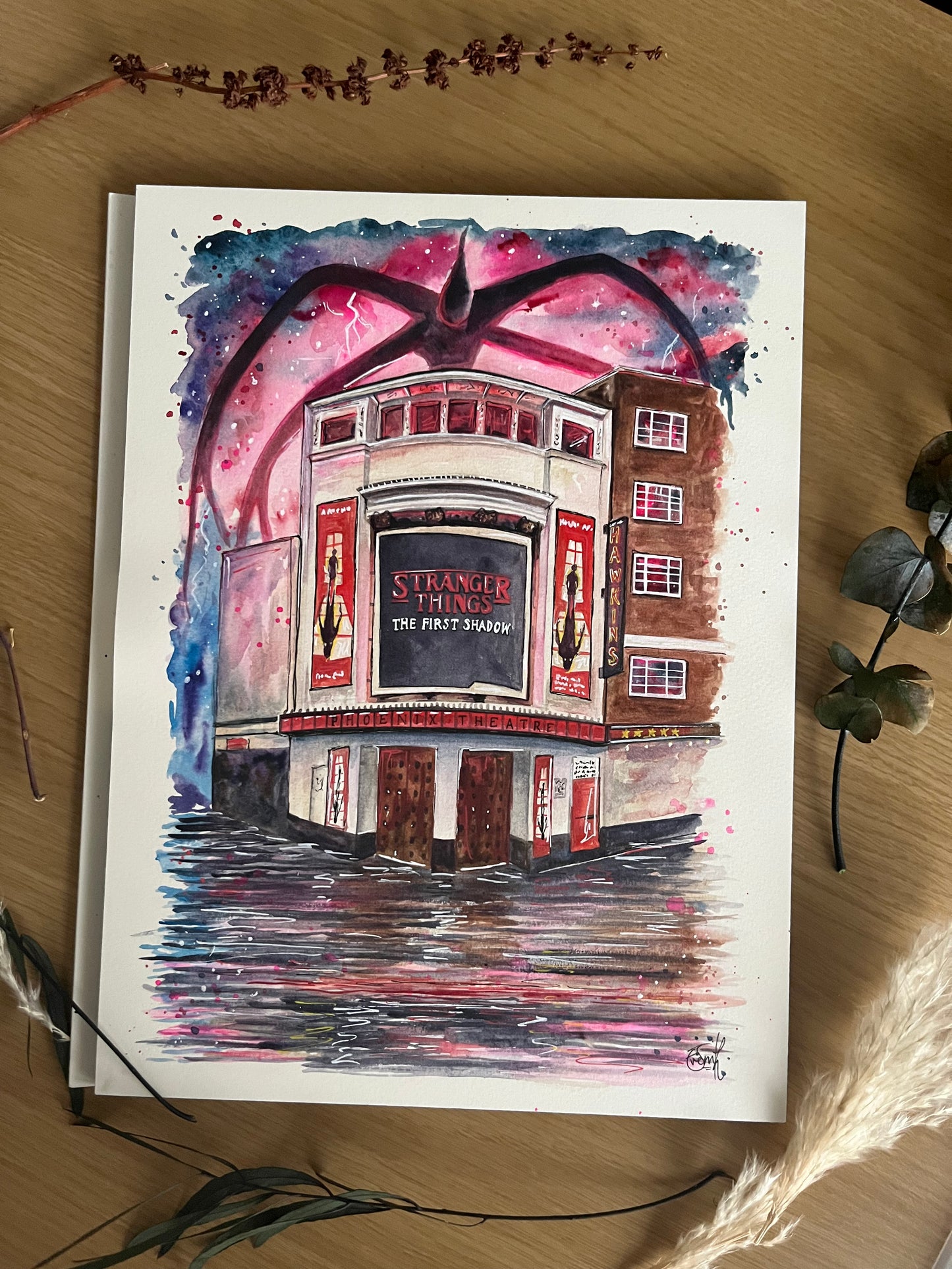 An Original watercolour illustration of the Phoenix Theatre in London’s West End. It features the ‘Stranger Things: The First Shadow’ marquee, with the water reflection if the mindflayer in the Upside Down. Painted by Eve Leoni Art.