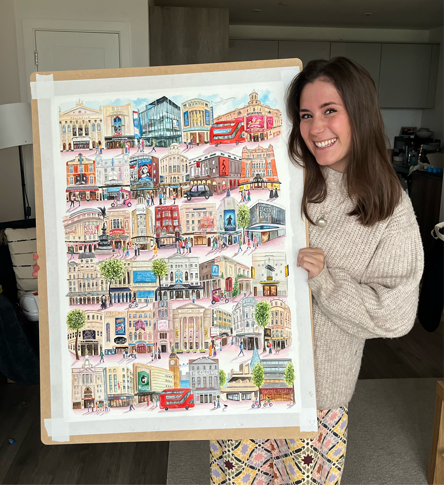 Watercolour artist, Eve Leoni Smith, holds up a large painting of the West End. It features 37 London theatres including the London Palladium, Piccadilly Theatre, Phoenix Theatre and Theatre Royal Drury Lane. 